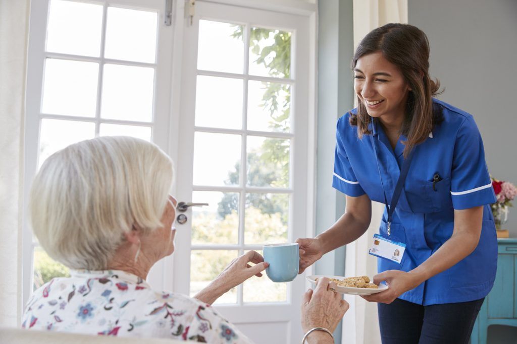 A care worker bringing a drink to an older woman at home